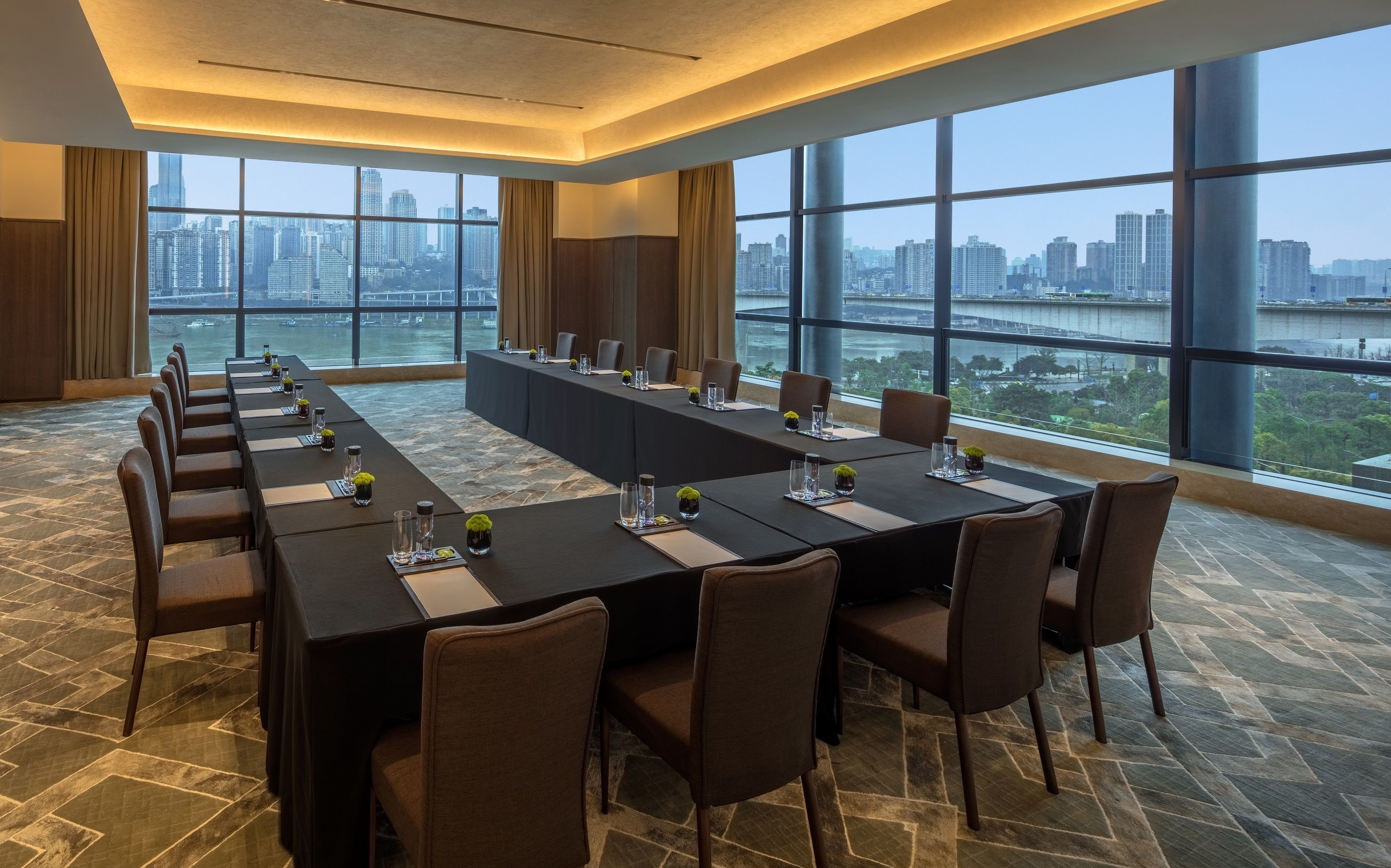 A conference room with a long table, chairs, and a city view through large windows.