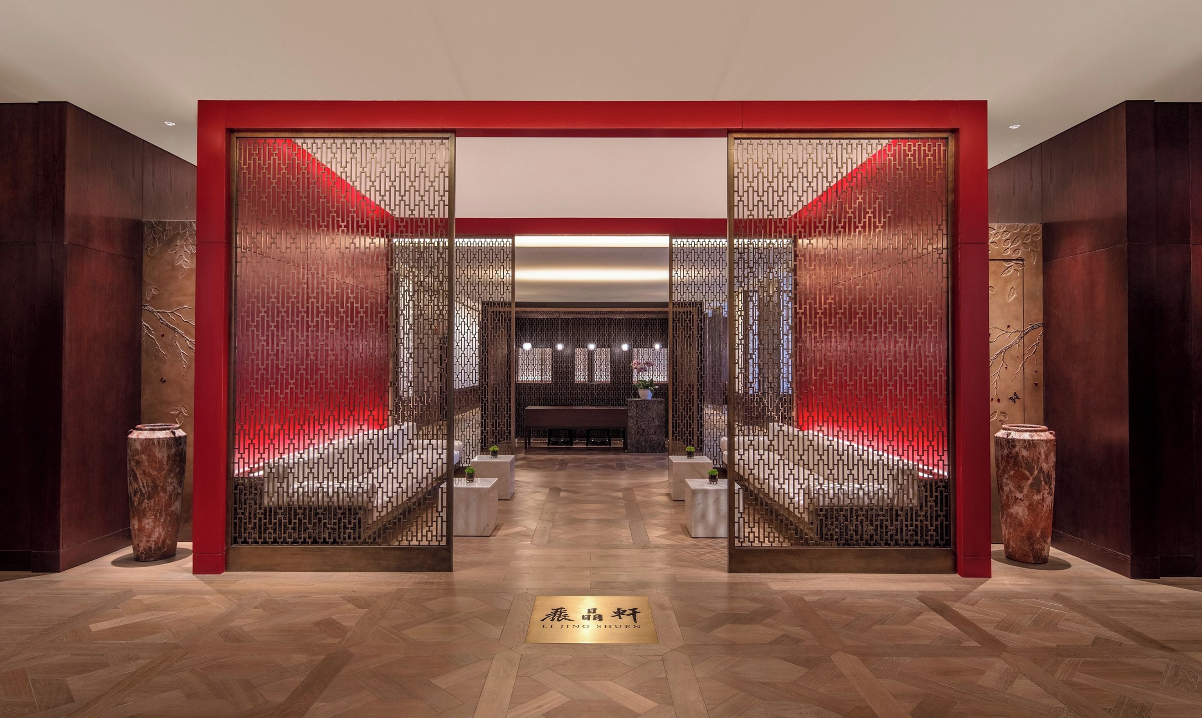 Vestíbulo de hotel con diseño tradicional, destacando una paleta de colores rojo y dorado, un banco central y una pared decorativa con intrincados diseños.