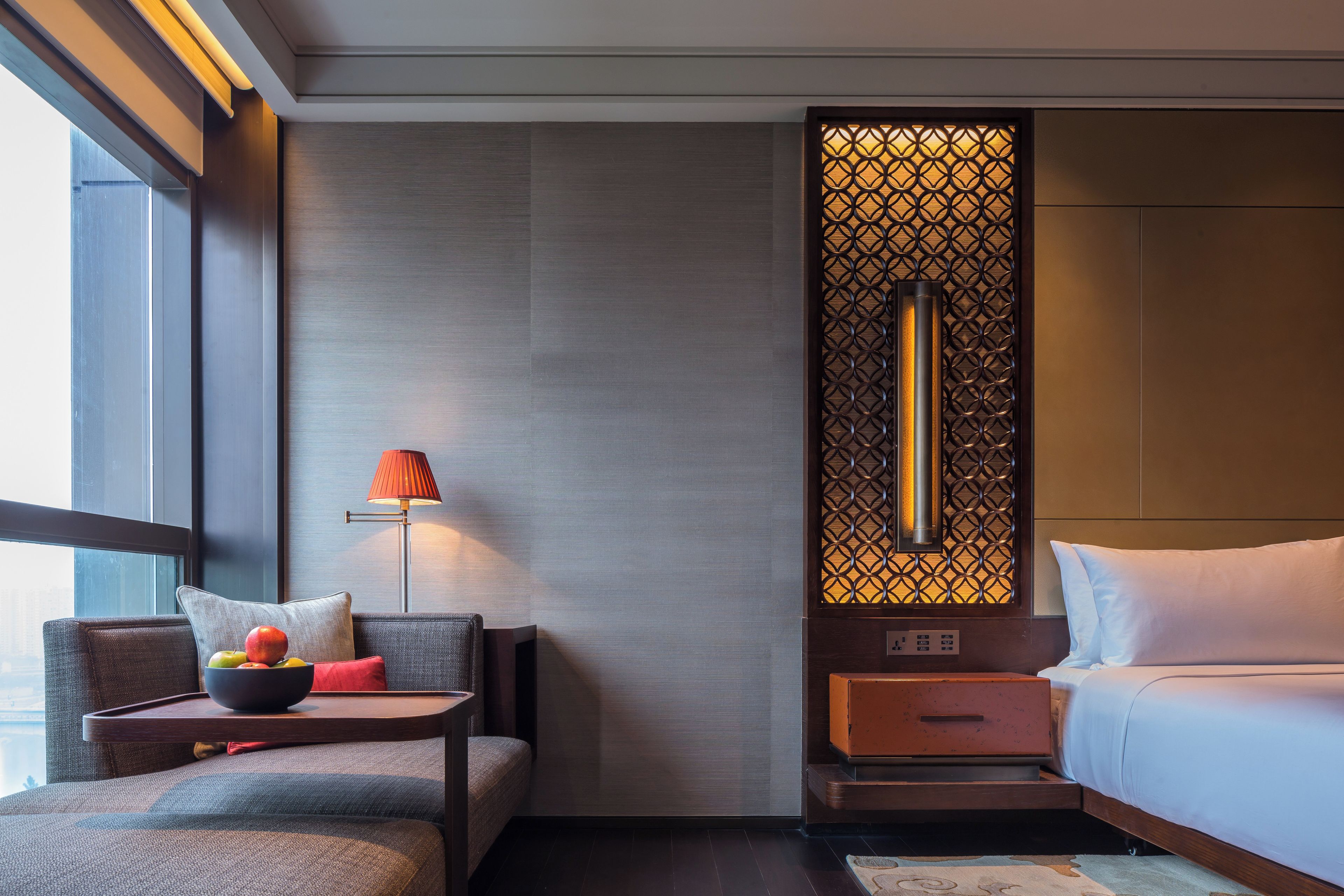 A modern hotel room with a sofa, bedside table, lamp, and a decorative screen.
