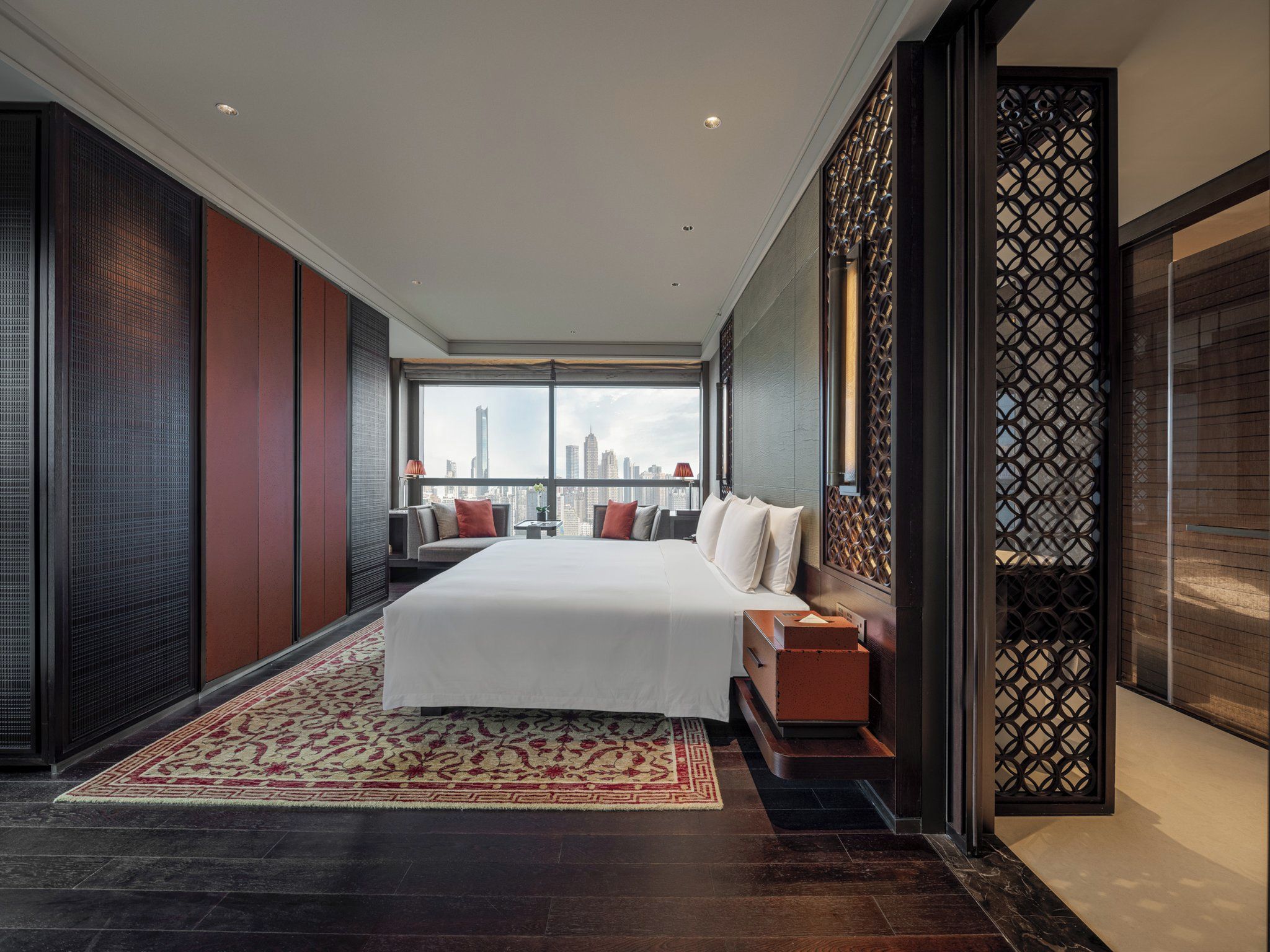 A modern hotel room with a large bed, a seating area, and a view of the city skyline.