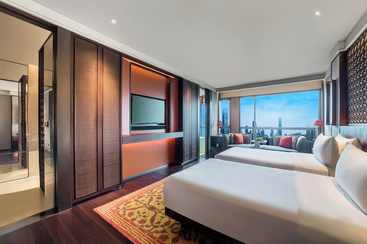 A modern hotel room with a large bed, a TV, and a city view.