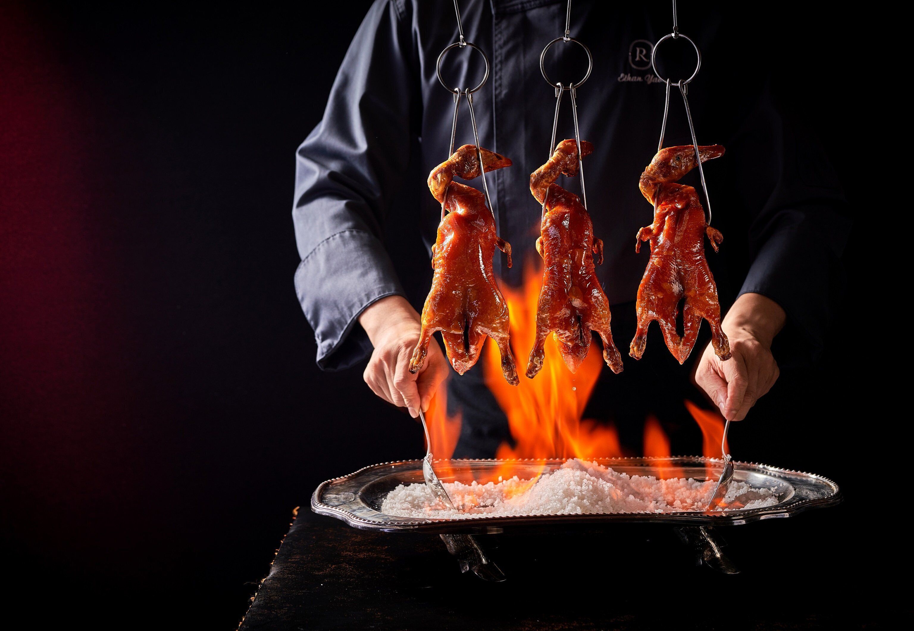 A person holding two roasted meats over a fire.