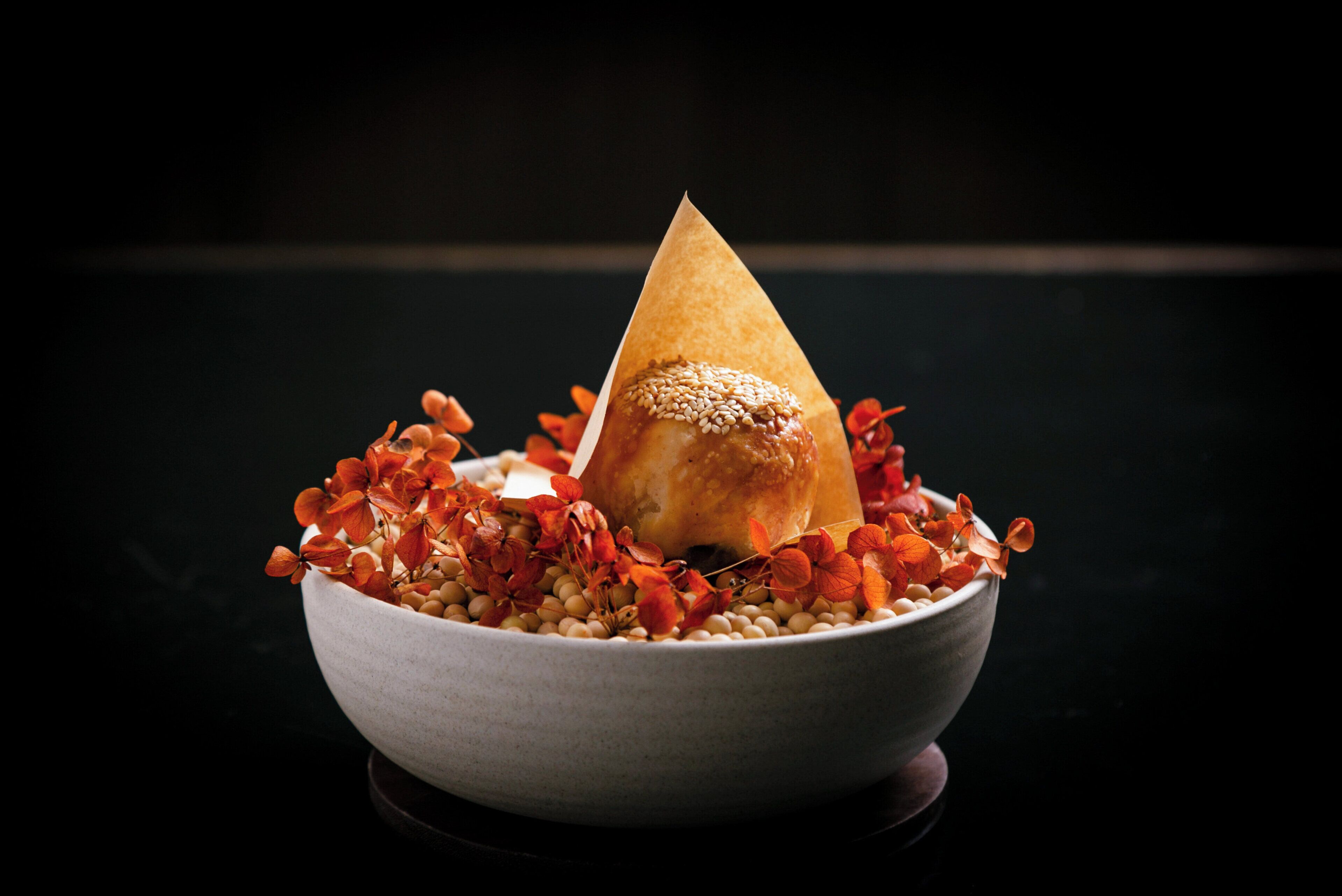 A bowl with a cone-shaped item on top, surrounded by red flowers and beans.