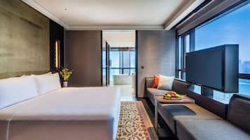A modern hotel room with a large bed, a sofa, a TV, and a balcony with a city view.