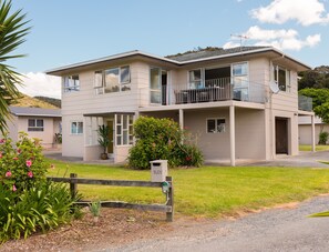 A two-story building with a balcony, a satellite dish, and a small garden area. - Waitangi Beach House (Paihia)