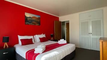 Une chambre à coucher avec un lit, une table de chevet, une lampe, un tableau et une armoire.