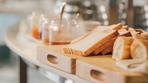 Een houten snijplank met sneetjes brood en een glazen pot met saus.