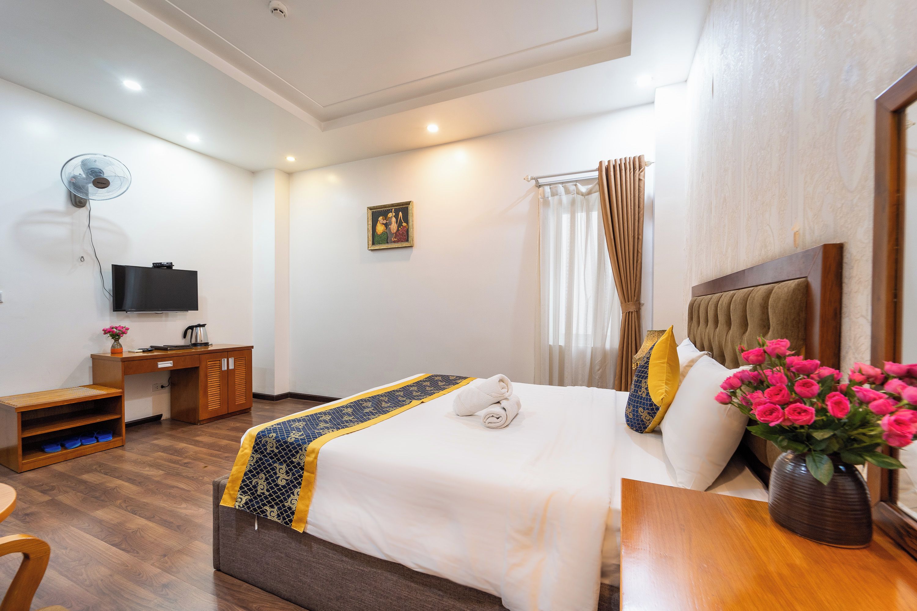 Una habitación de hotel con cama, escritorio, silla, televisor y ventana con cortinas.