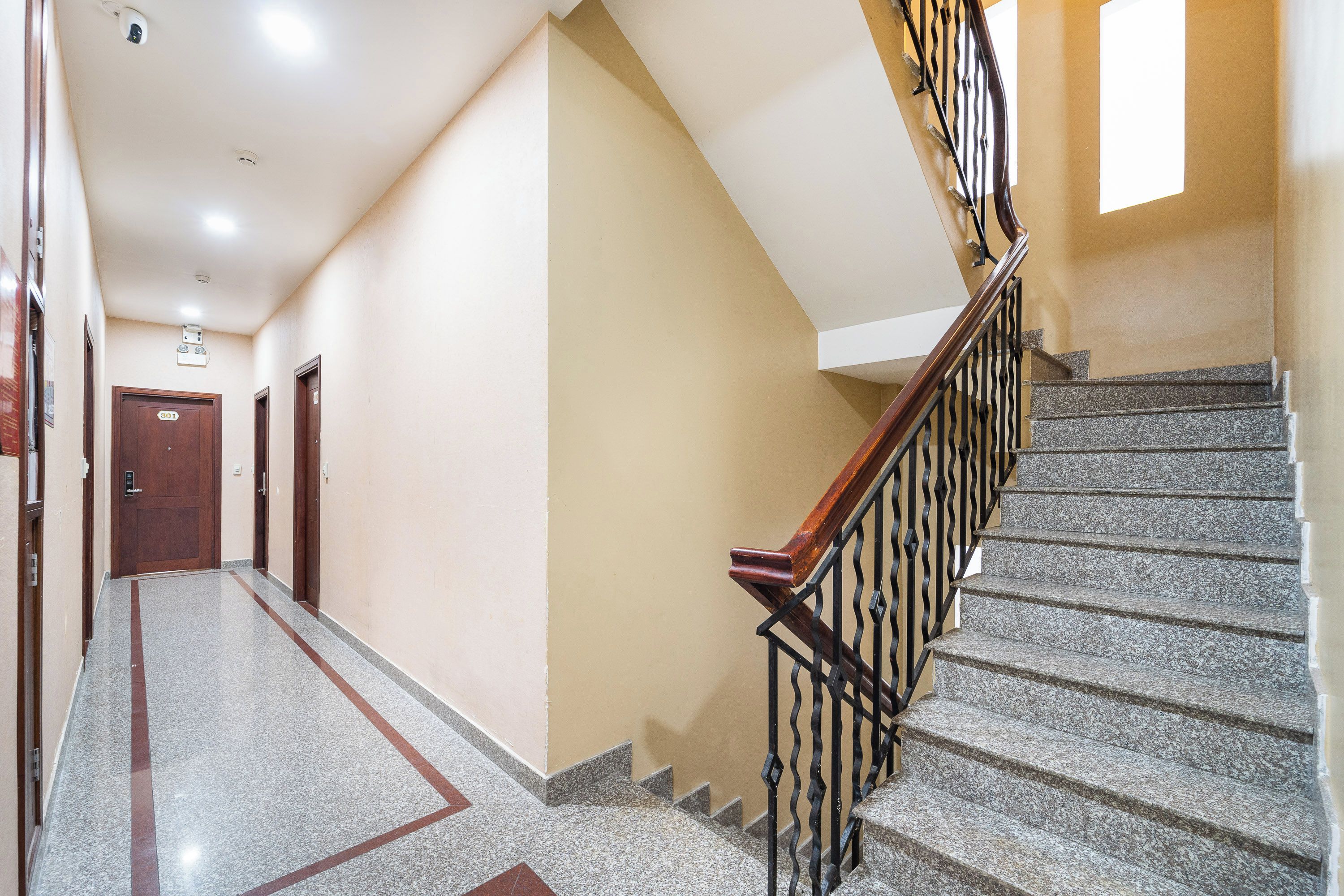 A hotel hallway with a marble floor, a wooden handrail, and a staircase with granite steps.