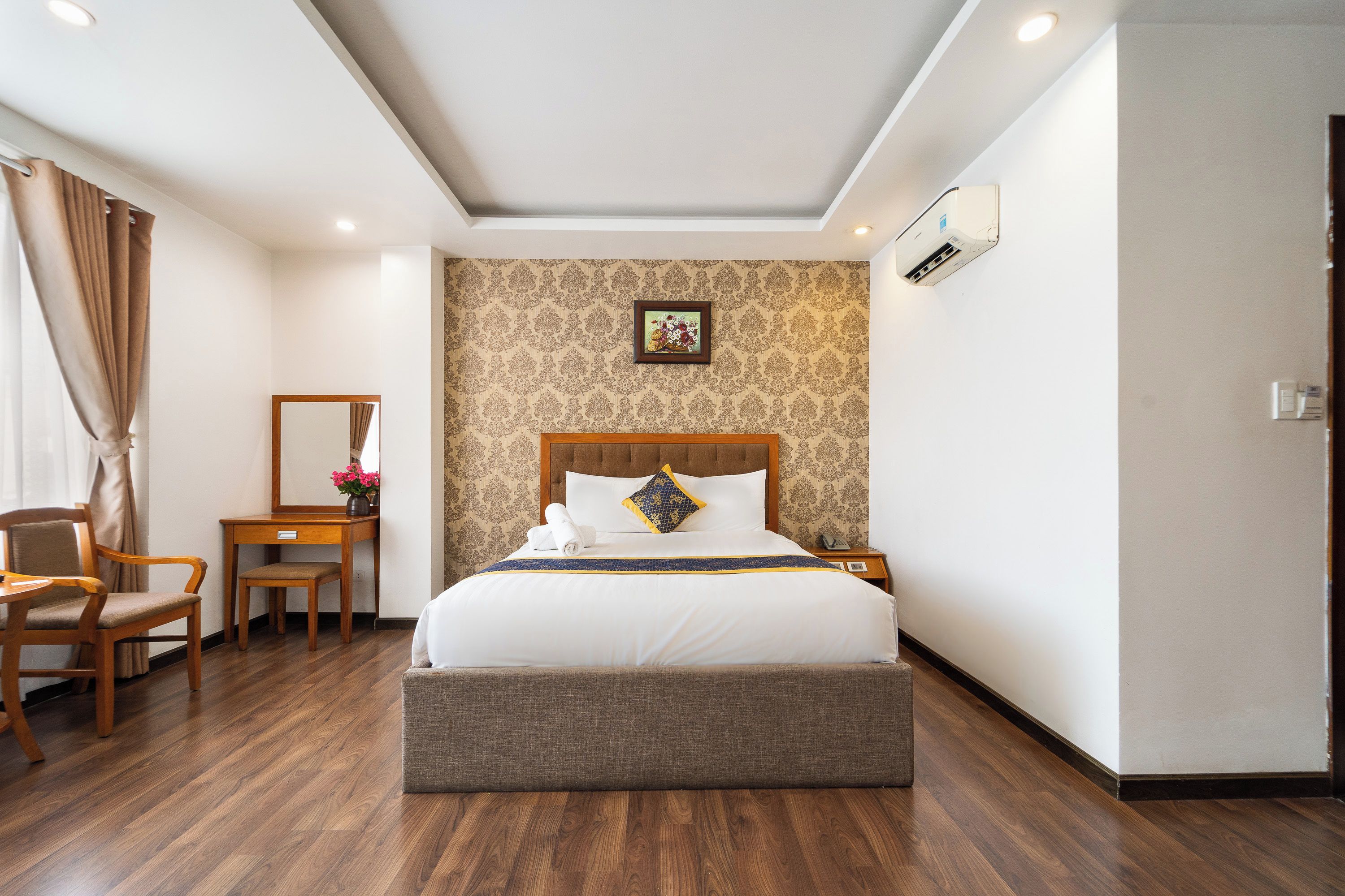 Una habitación de hotel con una cama grande, un escritorio de madera, una silla y un espejo.