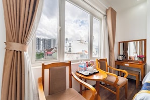 A hotel room with a large window, a dining table with chairs, a bed, and a desk with a mirror.