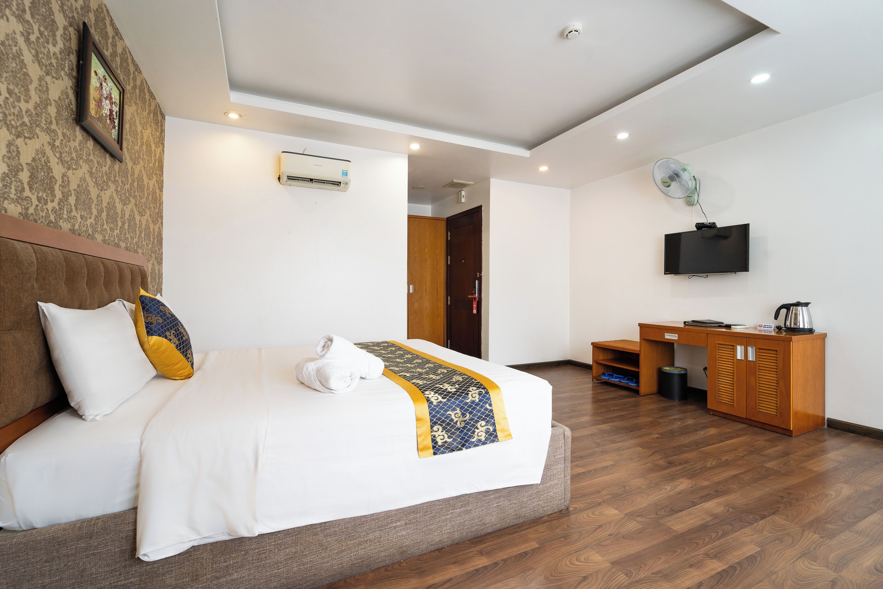 A hotel room with a bed, a desk, a television, and an air conditioning unit.