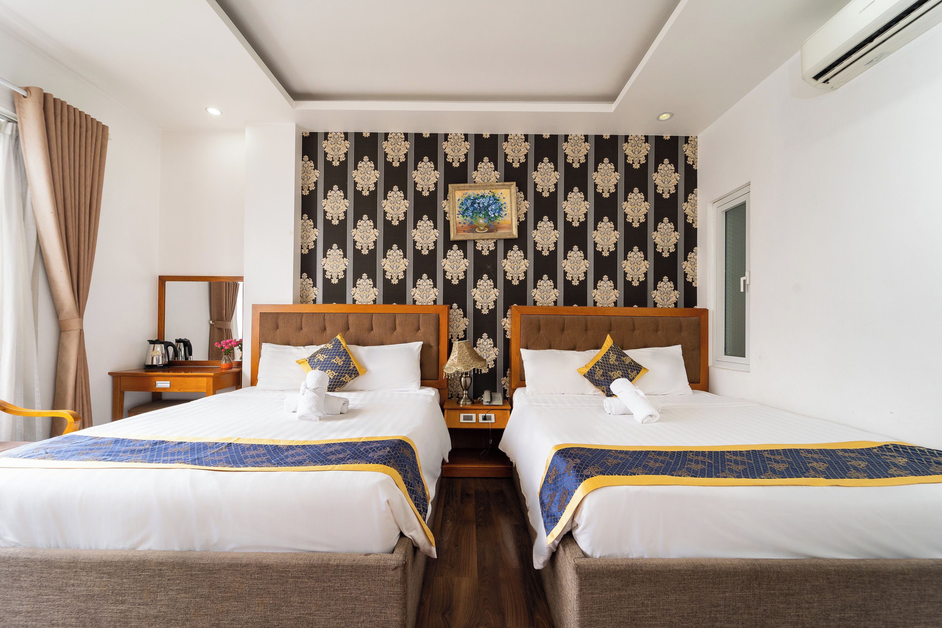 Habitación de hotel con dos camas, una mesita de noche, una lámpara y un cuadro en la pared.