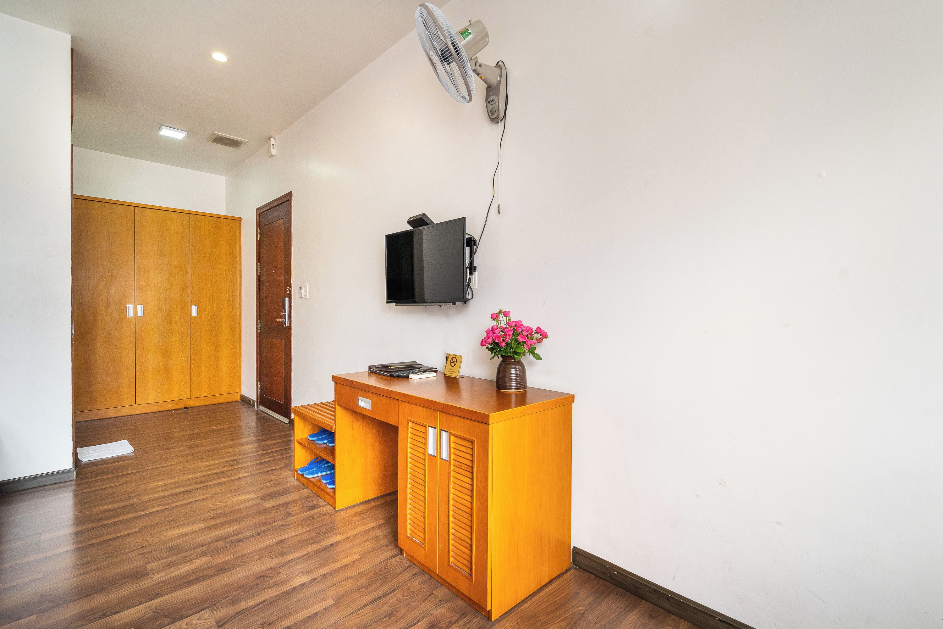 A reception desk with a flat-screen TV, a fan, and a vase with flowers.
