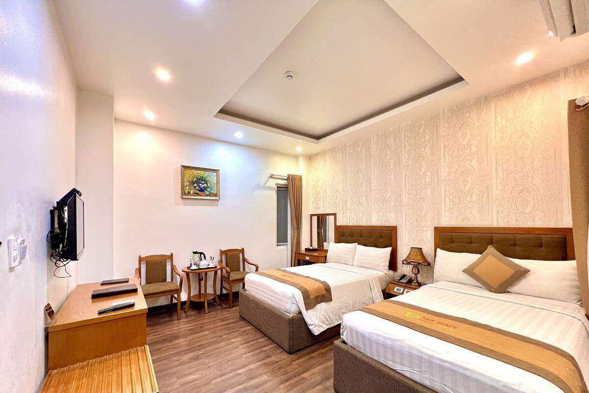 Une chambre d’hôtel avec deux lits, un bureau, une chaise, une petite table et un téléviseur.
