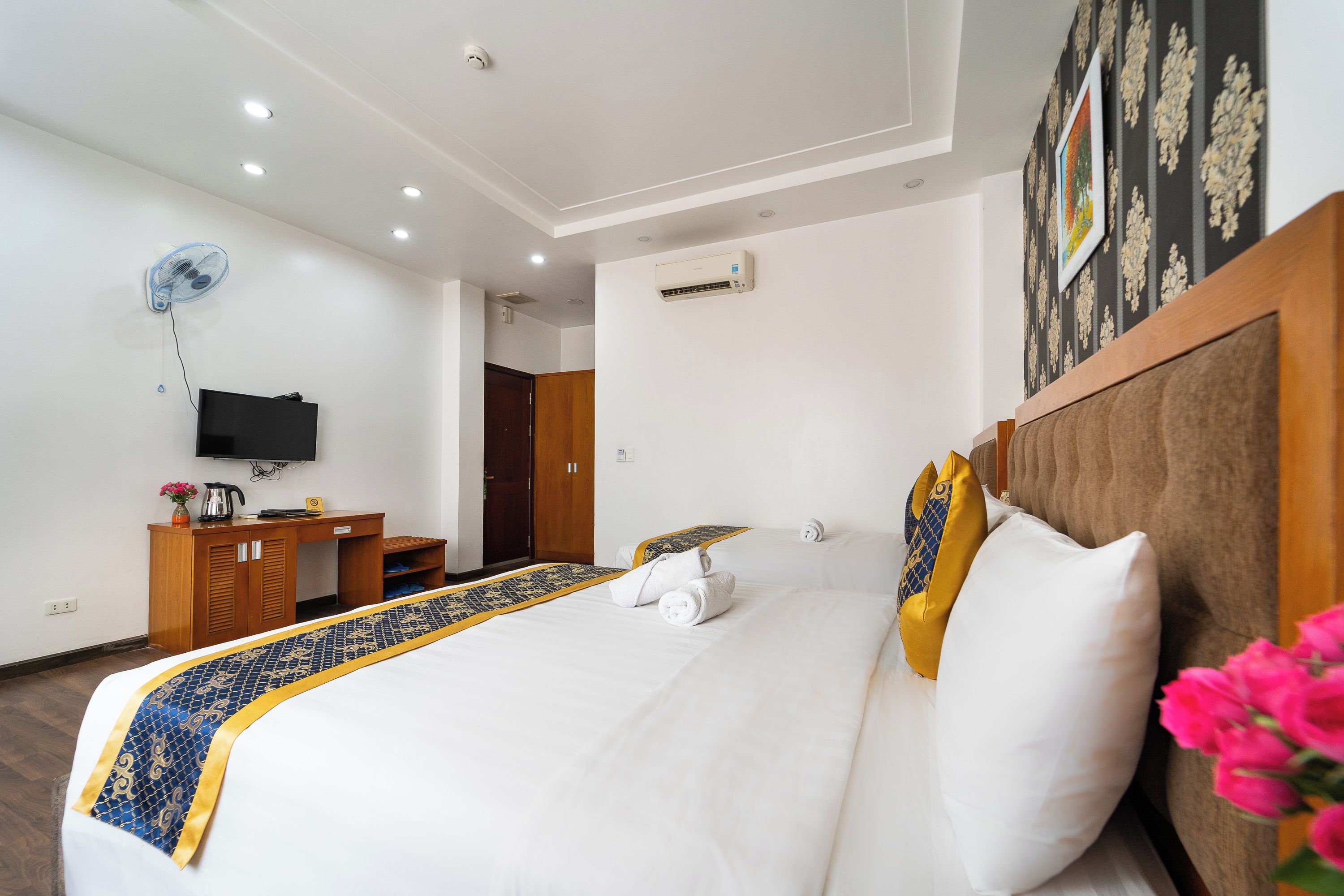 A hotel room with a bed, a desk, a television, and an air conditioning unit.