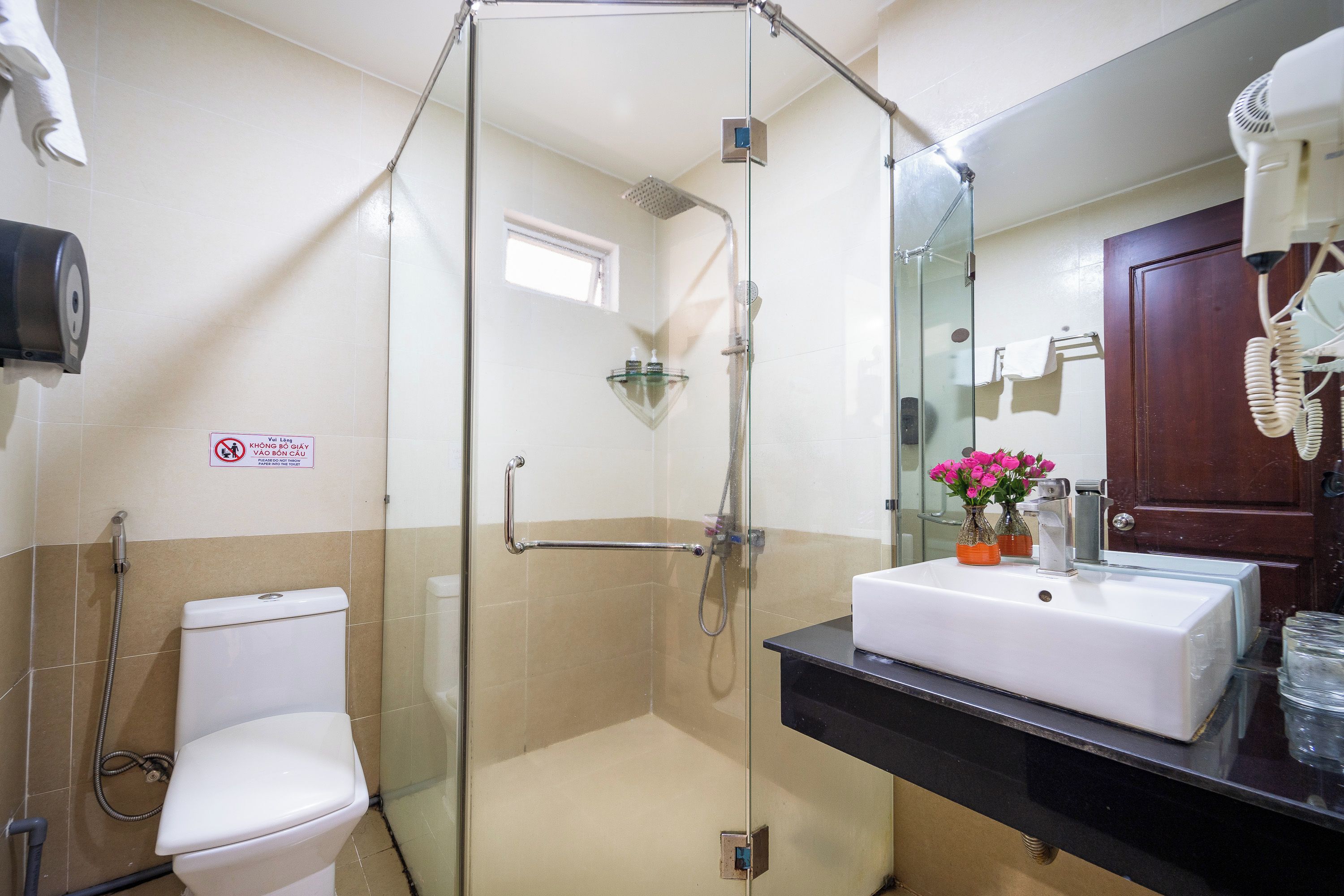 Un baño con ducha envuelta en vidrio, inodoro blanco y lavamanos con espejo superior.