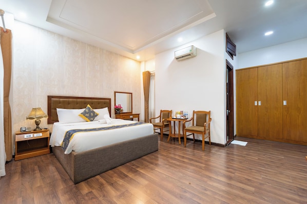 A hotel room with a bed, bedside table, lamp, mirror, and a wooden wardrobe.