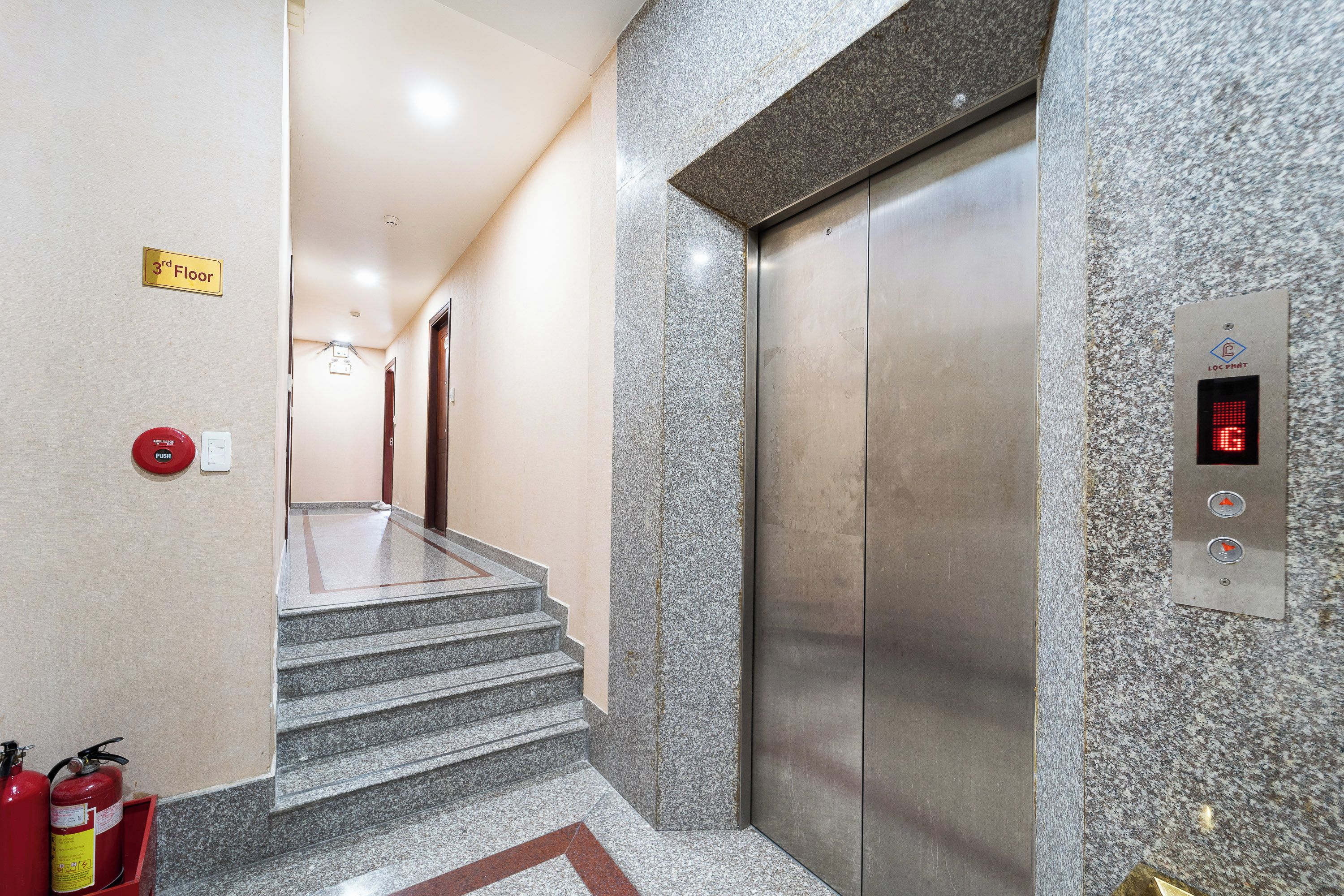 An elevator with a digital display, a push button, and a fire extinguisher on the wall.