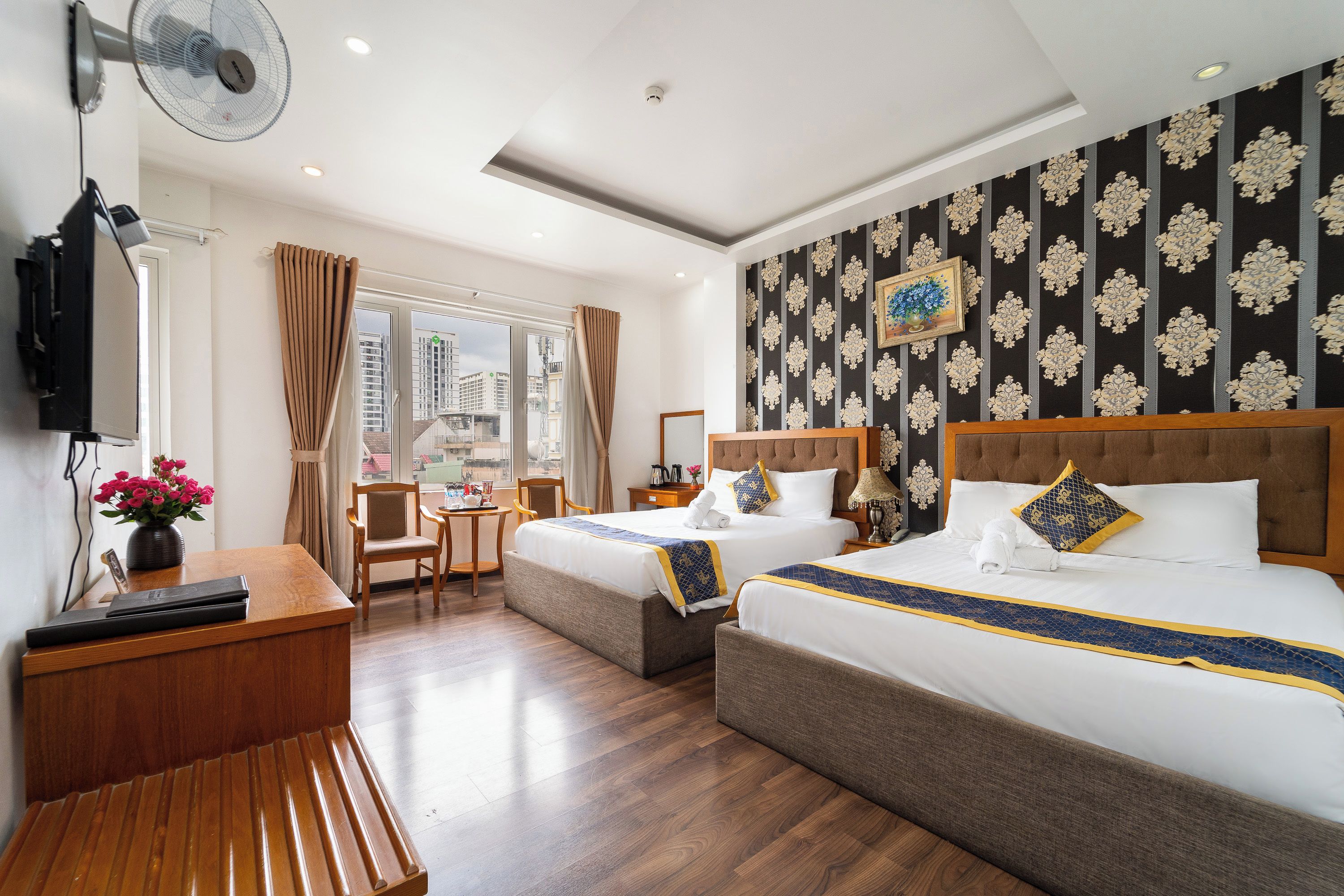 A hotel room with two beds, a desk, a chair, a television, and a window with a view of buildings.