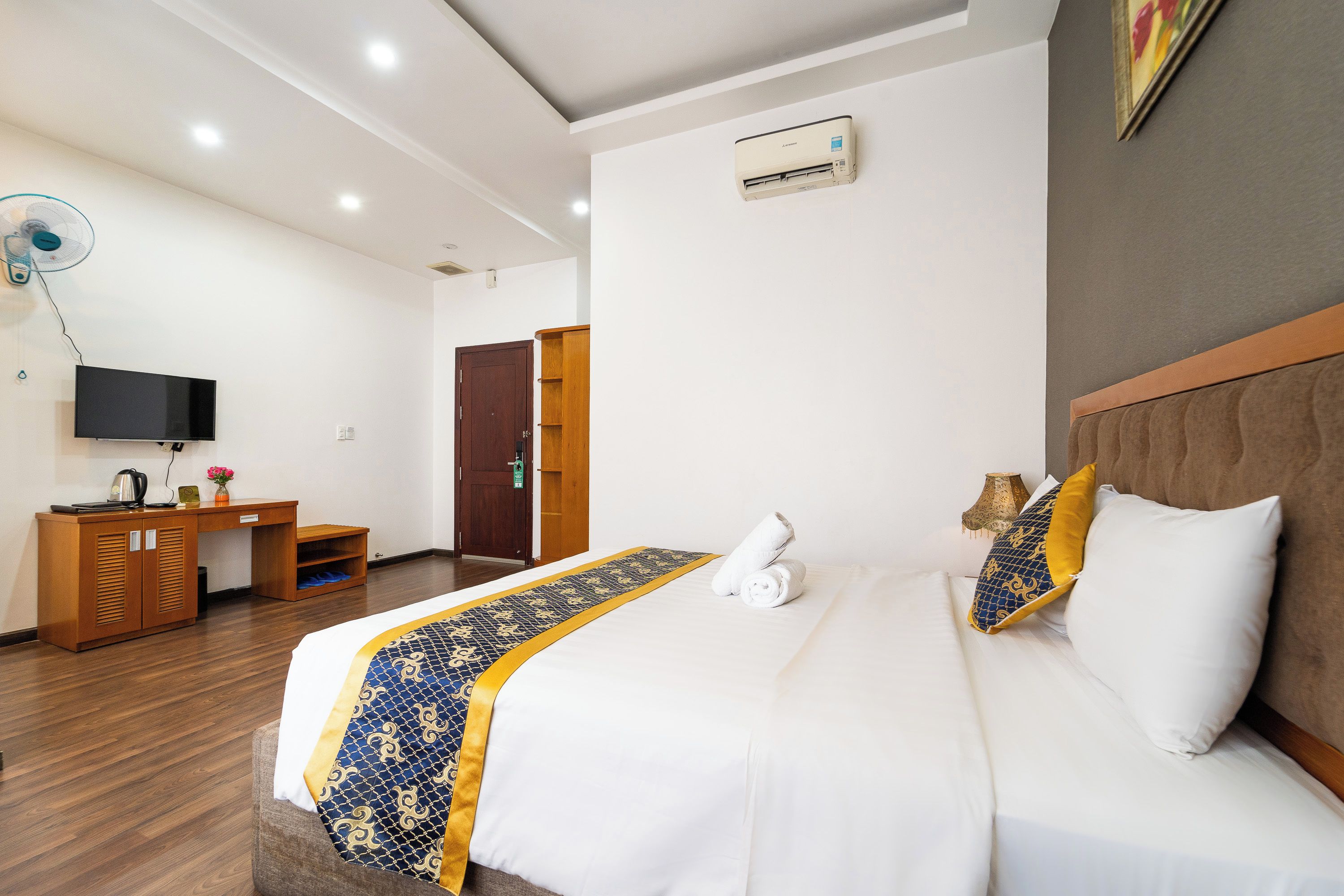 A hotel room with a bed, a desk, a television, and an air conditioning unit.