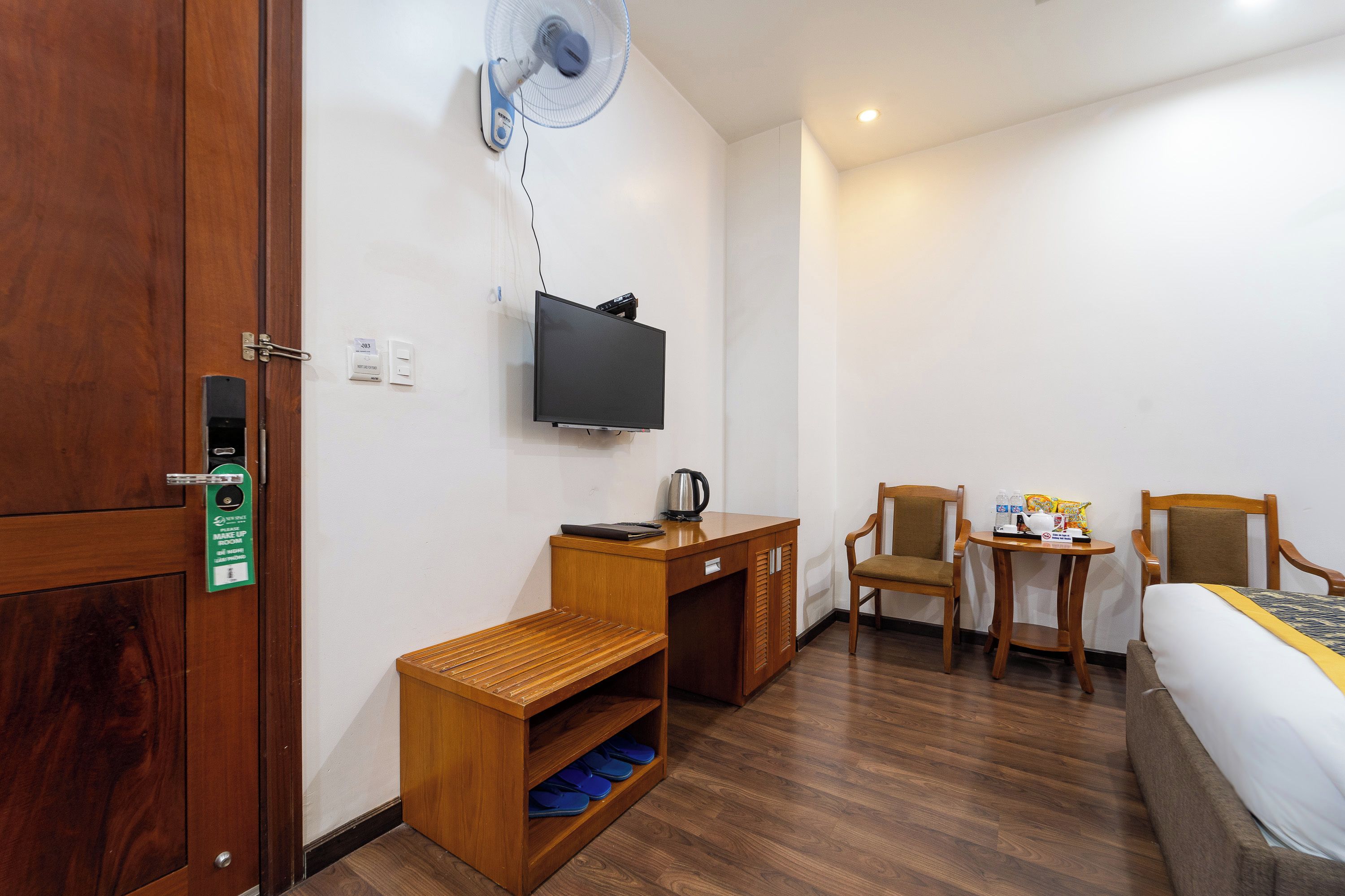 Une chambre d’hôtel avec un bureau en bois, un téléviseur fixé au mur, un lit, une chaise et une petite table sur laquelle se trouvent une bouilloire et quelques en-cas.