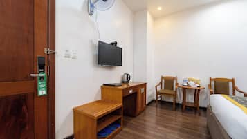 Une chambre d’hôtel avec un bureau en bois, un téléviseur fixé au mur, un lit, une chaise et une petite table sur laquelle se trouvent une bouilloire et quelques en-cas.