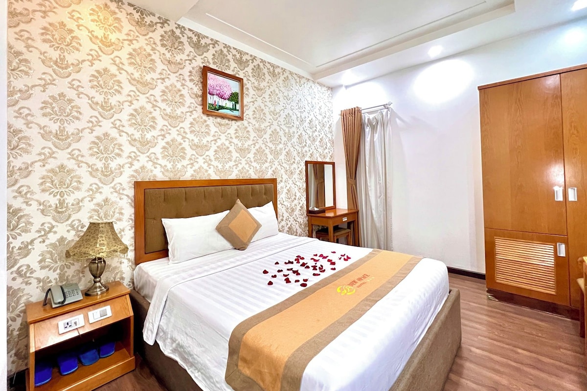 Una habitación de hotel con una cama grande, una mesita de noche con lámpara, un armario y un espejo decorativo.