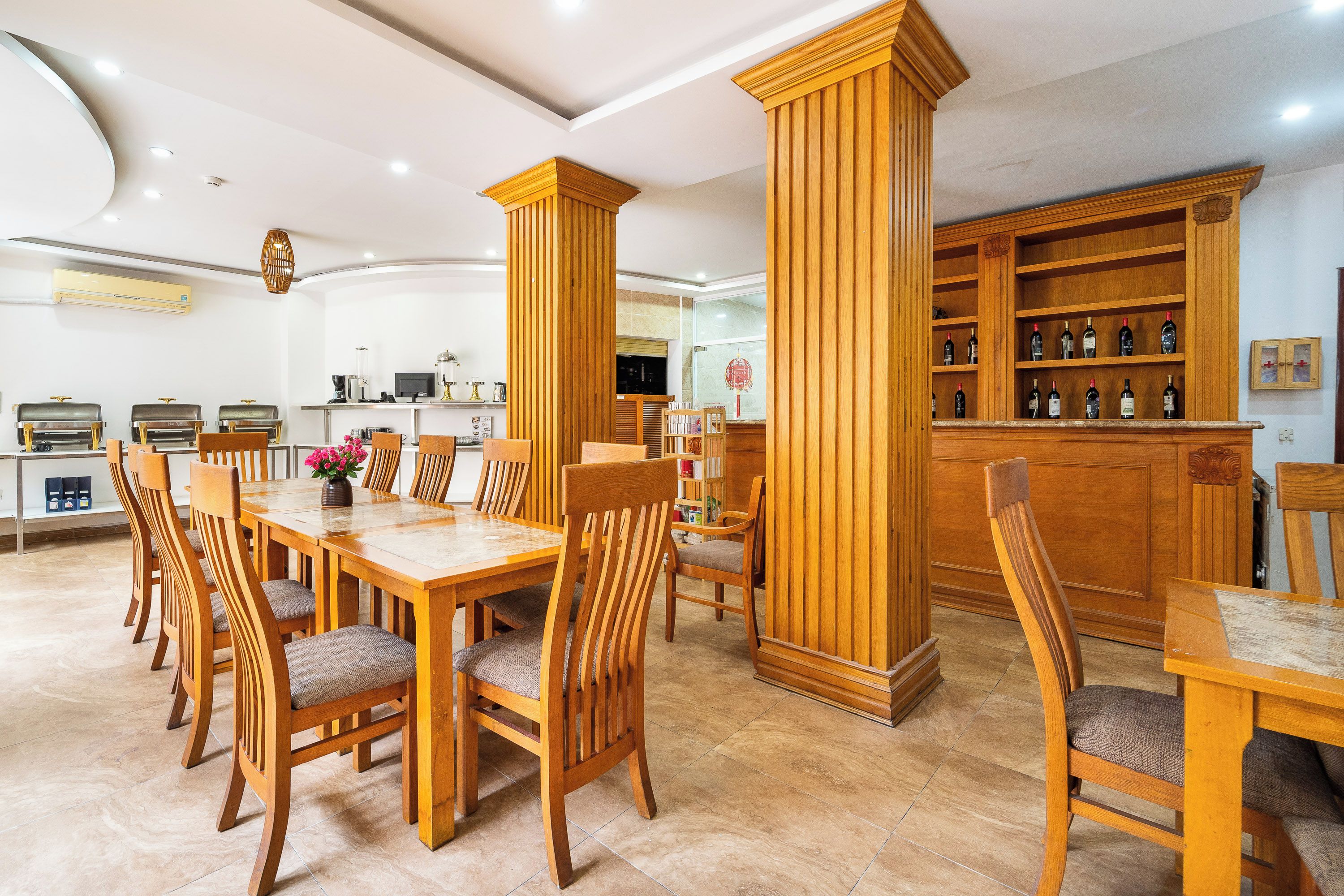 A dining area with wooden tables and chairs, a bar with shelves of bottles, and a kitchen in the background.