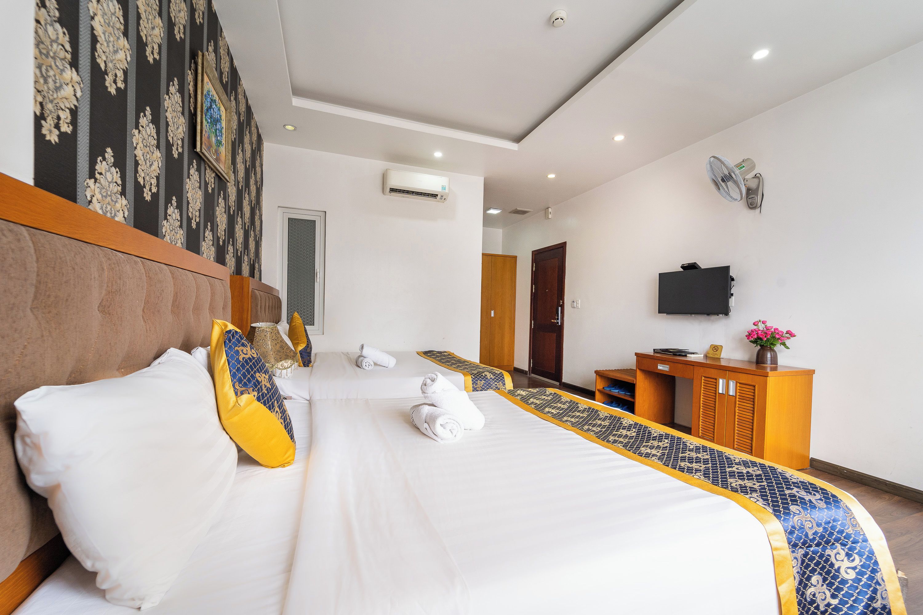 A hotel room with a bed, a desk, a TV, and an air conditioning unit.