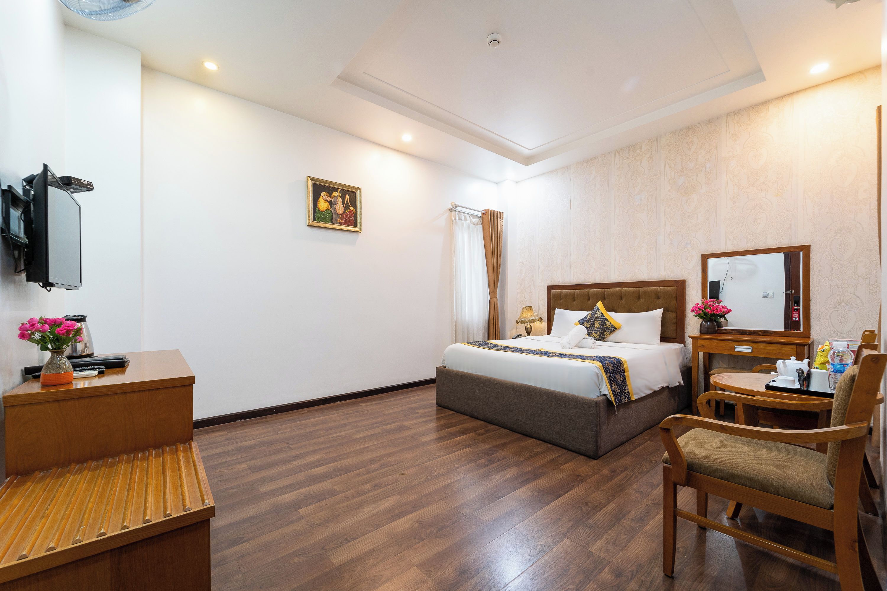 A hotel room with a bed, a desk, a chair, a TV, and a painting on the wall.