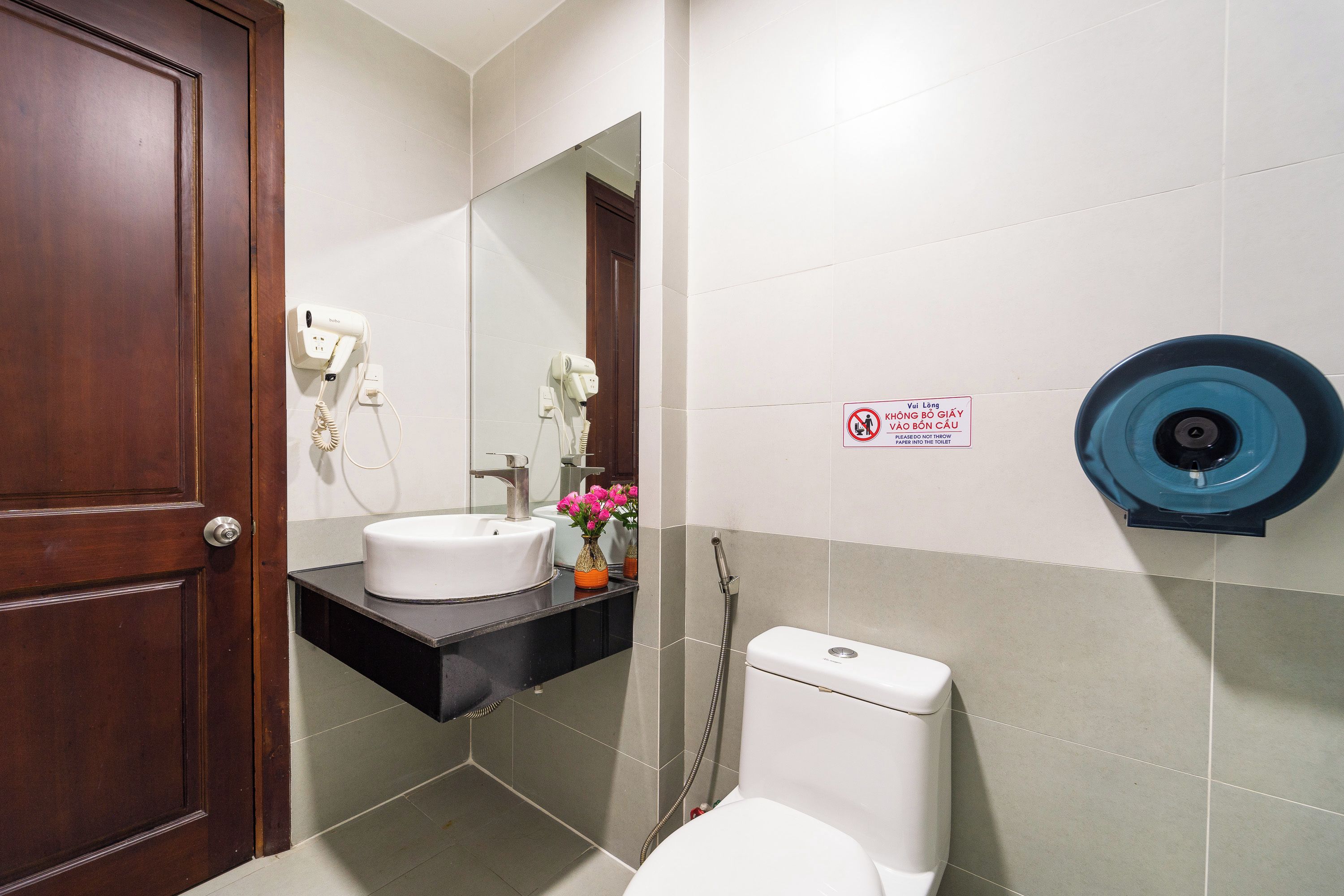 A bathroom with a wooden door, a white sink, a mirror, a toilet, and a blue toilet paper holder.