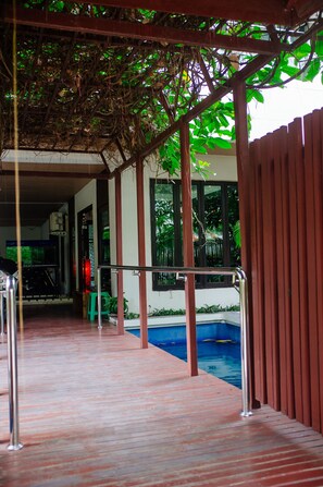 A covered outdoor area with a pool, wooden deck, and a metal railing. - Laidback Place Apartment (Bangkok)