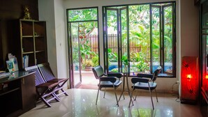A room with a glass door leading to a garden, a wooden cabinet, and a glass table with chairs. - Laidback Place Apartment (Bangkok)