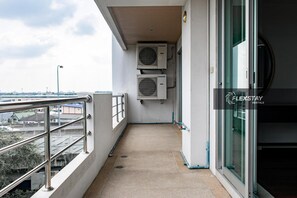 A balcony with a metal railing, two air conditioning units, a concrete floor, and a glass door. - Laidback Place Apartment (Bangkok)