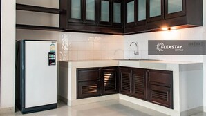 A modern kitchen with dark cabinetry, a white tiled backsplash, and a refrigerator. - Laidback Place Apartment (Bangkok)
