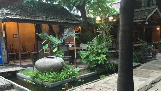 Un patio tradicional con fuente de agua, plantas en macetas y un edificio rústico con tejado de tejas.