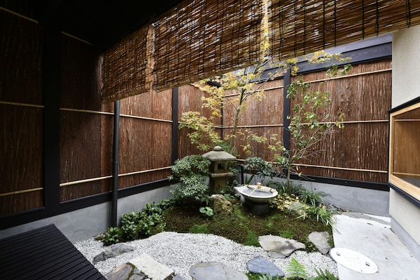 A traditional Japanese garden with a stone lantern, moss, rocks, and a bamboo fence.