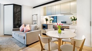 A modern living room with a grey sofa, white chairs, and a round table with a vase of flowers.