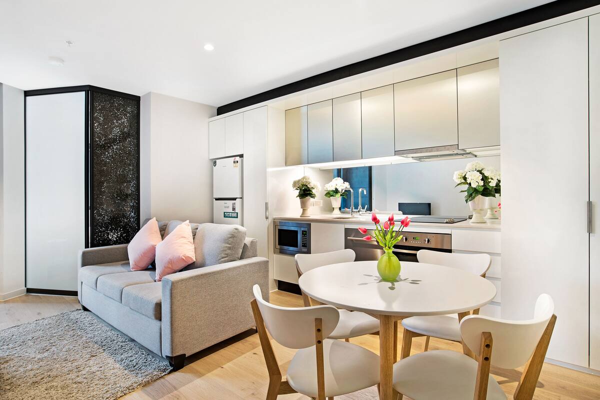 A modern living room with a grey sofa, white chairs, and a round table with a vase of flowers.