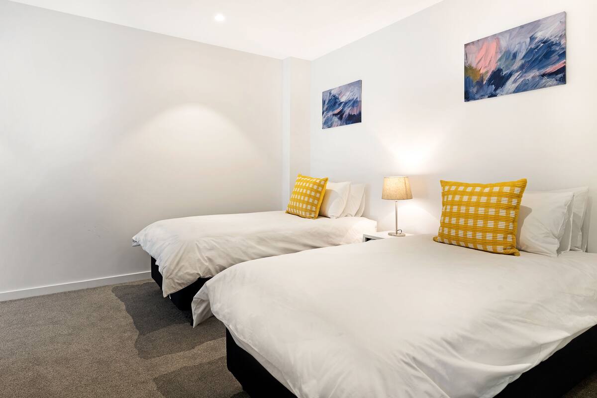 A hotel room with two beds, white bedding, and yellow patterned pillows.