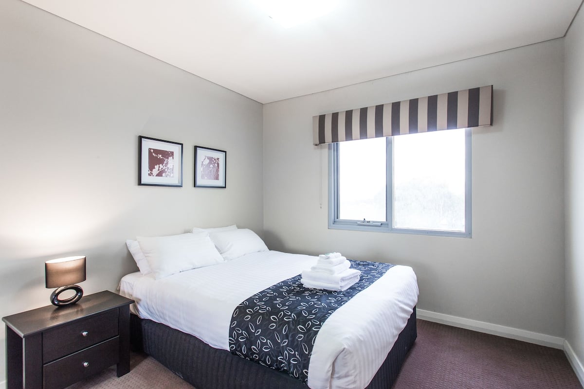 A neatly made bed with a striped valance, a bedside lamp, and two framed pictures on the wall.