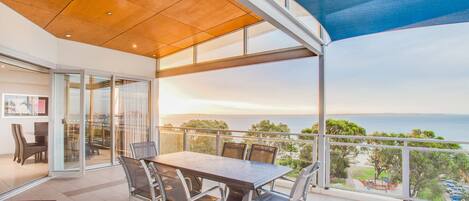 A balcony with a table and chairs, overlooking a scenic view of the sea and greenery.