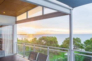 Un balcon avec vue sur la mer et les arbres au coucher du soleil.