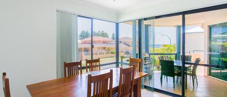 A dining area with a wooden table and chairs, large windows, and a view of the outside.