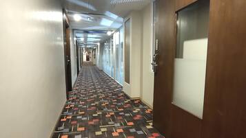 A hotel hallway with a patterned carpet, a wooden door with a sign indicating rooms 501-548, and a long corridor with doors on both sides.
