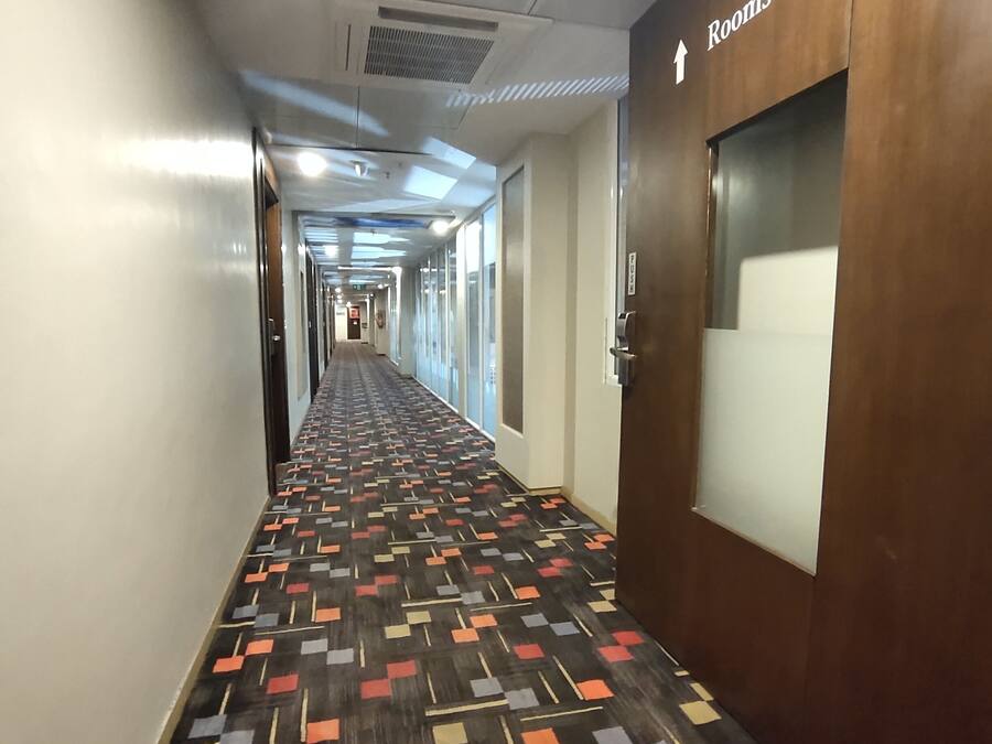 A hotel hallway with a patterned carpet, a wooden door with a sign indicating rooms 501-548, and a long corridor with doors on both sides.