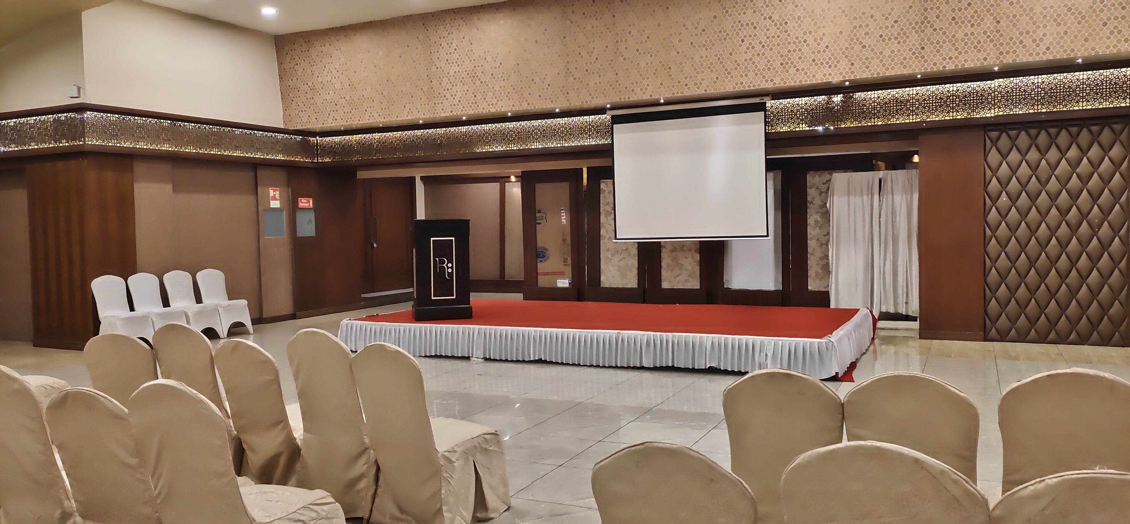 Une salle de conférence équipée d’une scène, de rangées de chaises et d’un écran de projection.