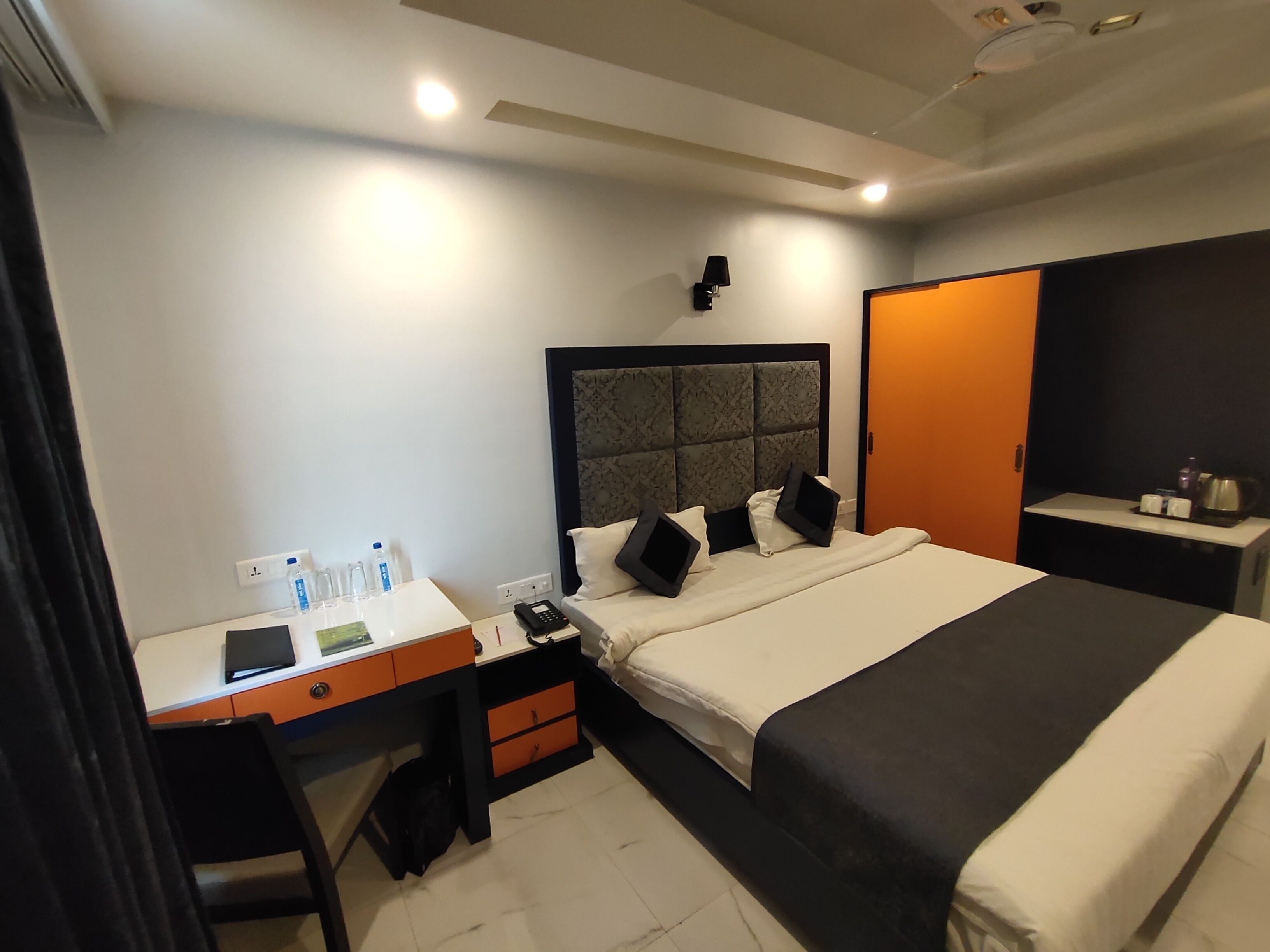 Une chambre d’hôtel comprenant un lit, un bureau, une chaise, une armoire et une table de chevet avec une lampe.