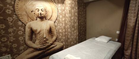 Ein Zimmer mit einer großen Buddha-Statue an der Wand, einem Bett mit weißer Matratze und Kissen sowie einem Holzboden.